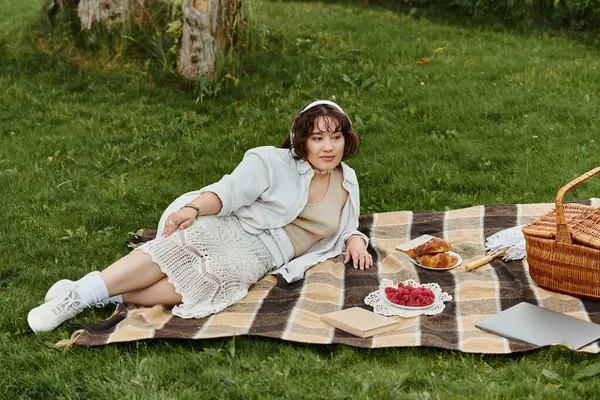 A young woman in a white shirt relaxes on a blanket, surrounded by delicious picnic treats under the summer sun. — Stock Photo
