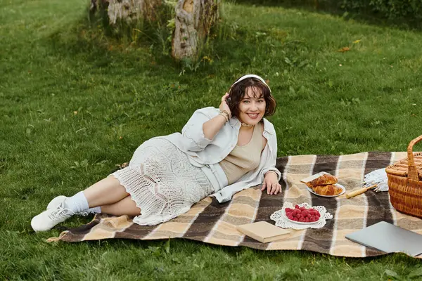 A young woman in a white shirt rests on a picnic blanket, savoring summer vibes with food and nature. — Stock Photo