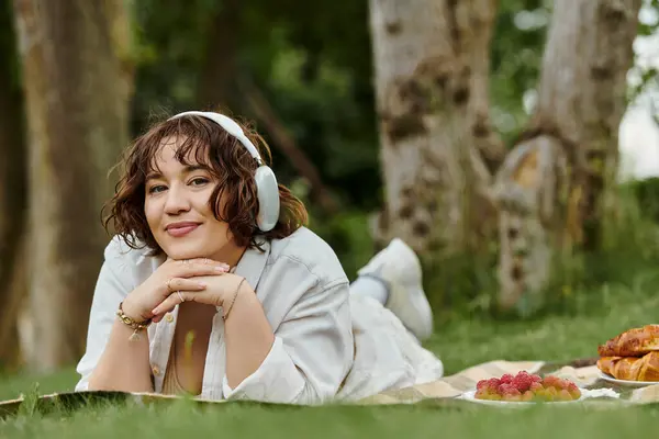 A cheerful woman enjoys a sunny summer day, resting on a picnic blanket surrounded by delicious treats. — Stock Photo