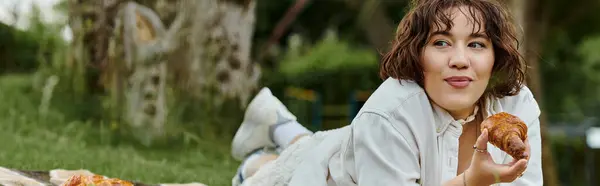 A young woman in a white shirt relaxes outdoors, savoring a delicious pastry under the warm summer sun. — Stock Photo