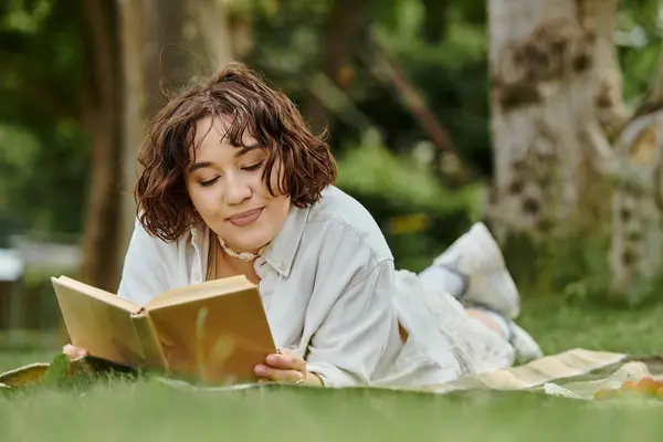 Une jeune femme se prélasse sur une couverture, immergée dans un livre, se prélassant dans la chaleur d'une journée d'été. — Photo de stock