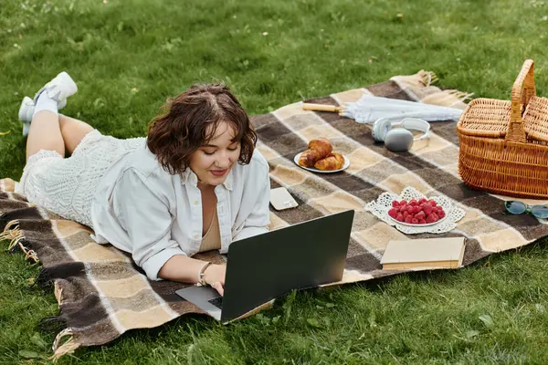 A young woman enjoys a peaceful summer picnic, resting on a blanket while using her laptop outdoors. — Stock Photo