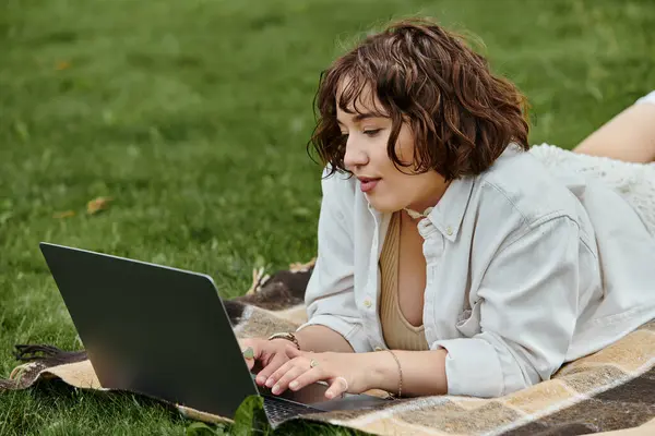 A young woman in a white shirt takes a break on a sunny day, working on her laptop during a summer picnic. — Stock Photo