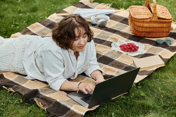 A young woman relaxes on a picnic blanket, working on her laptop amidst a bright summer day. — Stock Photo