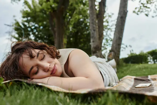 A young woman enjoys a peaceful moment while resting on a picnic blanket surrounded by nature. — Stock Photo