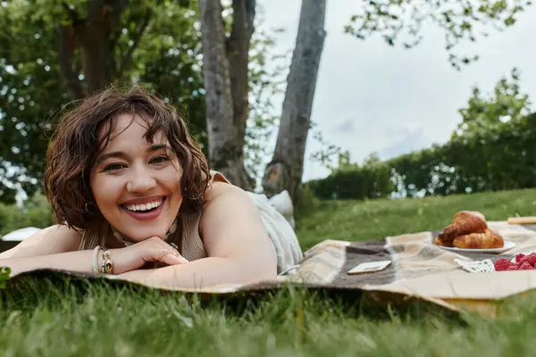 A young woman in a white shirt relaxes on a picnic blanket, basking in the warmth of a sunny summer day. — Stock Photo