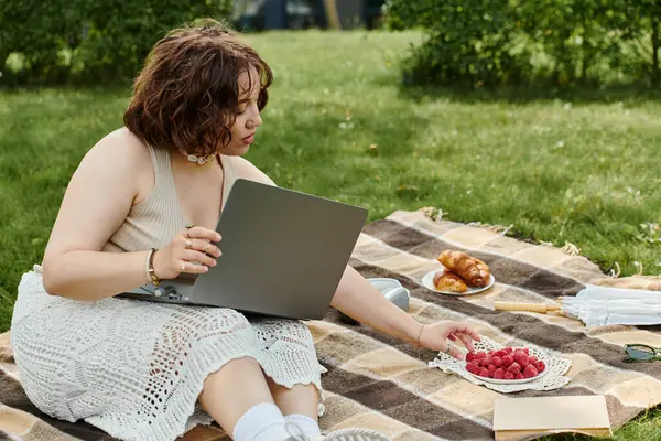 A young woman relaxes on a picnic blanket, savoring fresh raspberries while enjoying a sunny summer afternoon. — Stock Photo