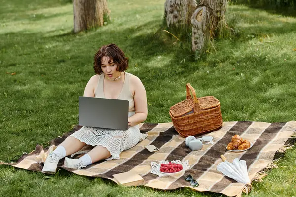 A young woman in a white shirt enjoys a summer picnic while working on her laptop in the sun. — Stock Photo