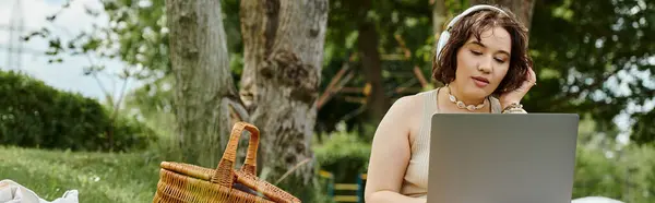A young woman in a white shirt relaxes at a summer picnic, working on her laptop and enjoying the day. — Stock Photo