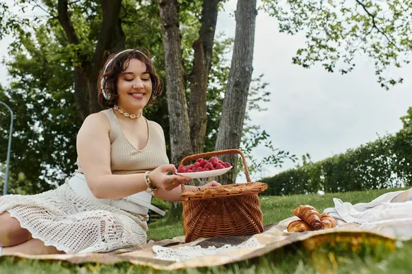 A young woman in a white shirt happily enjoys a summer picnic, surrounded by nature and vibrant fruits. — Stock Photo