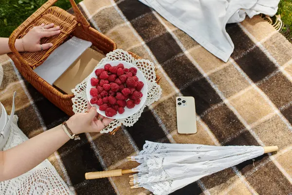 A young woman in a white shirt relaxes during a summer picnic, savoring fresh raspberries on a blanket. — Stock Photo