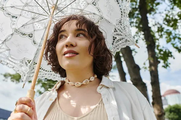 Una giovane donna con i capelli ricci sorride mentre si rilassa in un parco lussureggiante in una giornata estiva soleggiata. — Foto stock