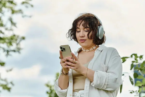 A pretty young woman in a white shirt savoring music while relaxing outdoors in a vibrant green park. — Stock Photo
