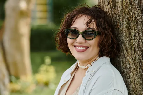 A cheerful young woman relaxes in a lush green park, savoring the warmth of a summer day. — Stock Photo