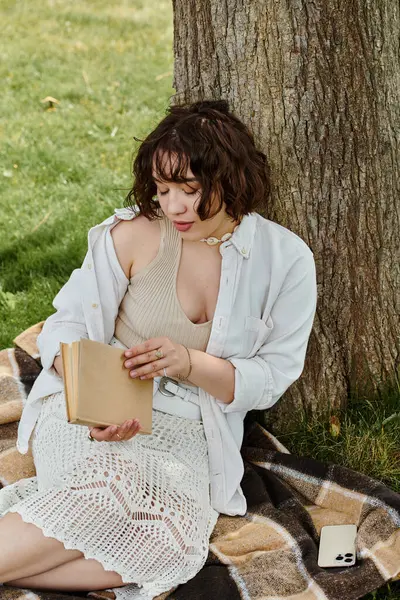 A young woman relaxes outdoors, immersed in her book, surrounded by vibrant greenery on a sunny day. — Stock Photo