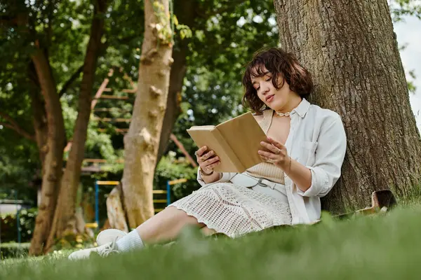 Молодая женщина любит читать книгу под деревом в пышном летнем парке. — стоковое фото