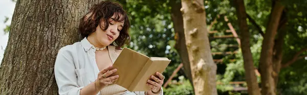 A young woman enjoys reading a book while relaxing in a vibrant green park on a warm summer day. — Stock Photo