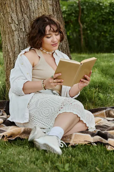 A young woman relaxes under a tree, absorbed in her book, surrounded by lush greenery and summer sunshine. — Stock Photo
