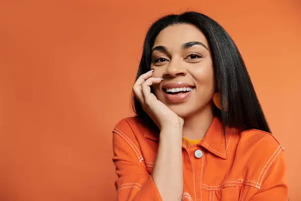 Mujer alegre expresa alegría con una sonrisa cálida sobre un fondo naranja vibrante. - foto de stock