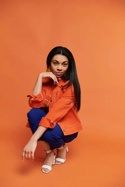 A poised woman showcases her style in a vivid orange environment. — Stock Photo