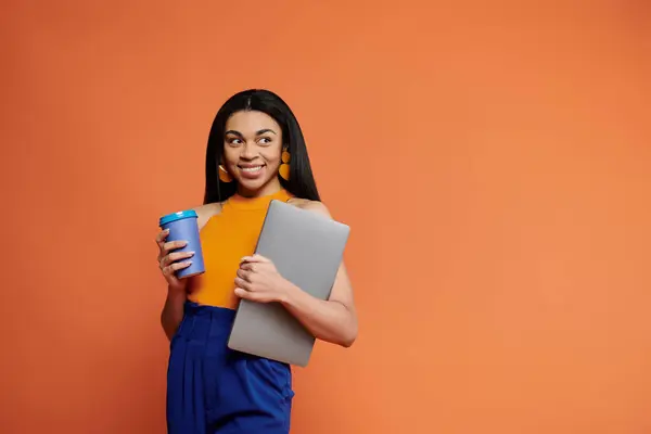 Woman smiles warmly, clutching a laptop and coffee cup in a bright setting. — Stock Photo