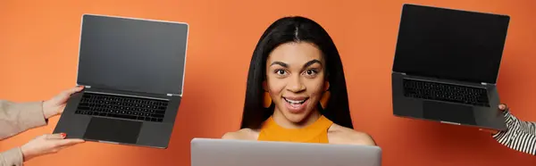 A cheerful woman joyfully interacts with multiple laptops in a lively setting. — Stock Photo