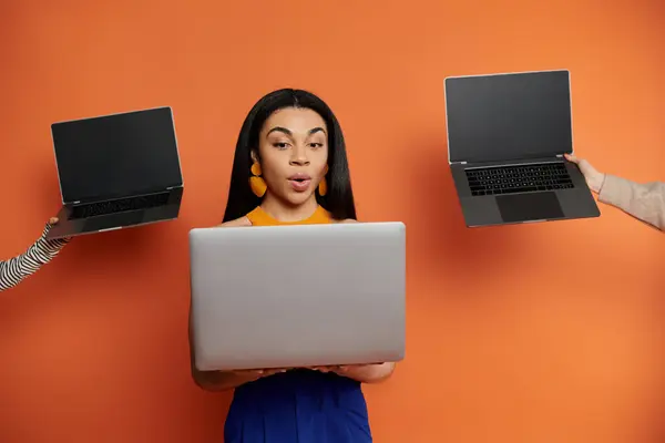 Uma mulher interage entusiasticamente com três laptops em um ambiente animado. — Fotografia de Stock