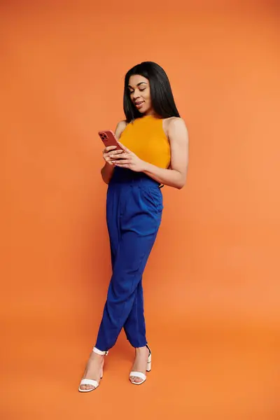 A stylish woman enjoys texting while standing confidently in vibrant attire. — Stock Photo