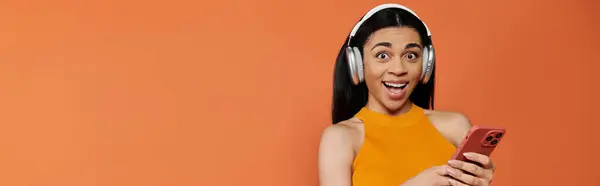 A vibrant woman smiles widely while listening to music on her phone. — Stock Photo