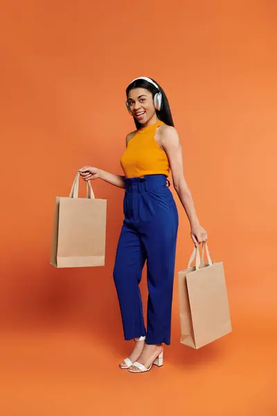 Elle rayonne de joie tout en tenant fièrement des sacs à provisions et en portant des écouteurs. — Photo de stock