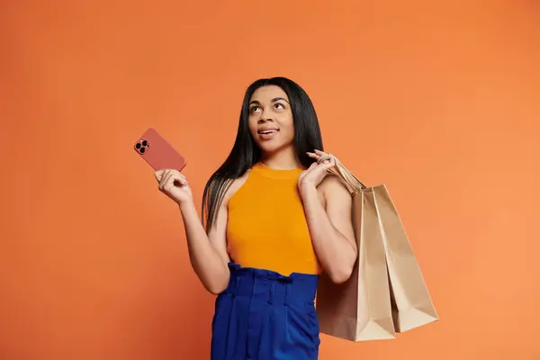 A stylish woman holds shopping bags and a phone, radiating excitement. — Stock Photo