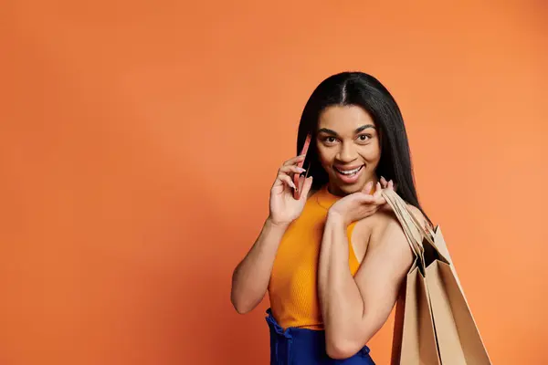 A cheerful woman engages in a phone call while holding shopping bags. — Stock Photo