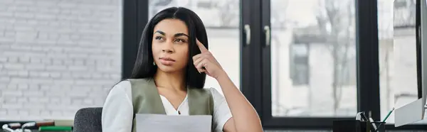 A thoughtful woman reflects while seated in a bright workspace. — Stock Photo