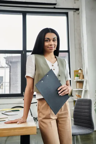 Una donna in bilico si alza orgogliosa, tenendo una cartella nel suo ufficio elegante. — Foto stock