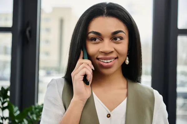 A smiling woman talks on the phone while surrounded by a modern workspace. — Stock Photo