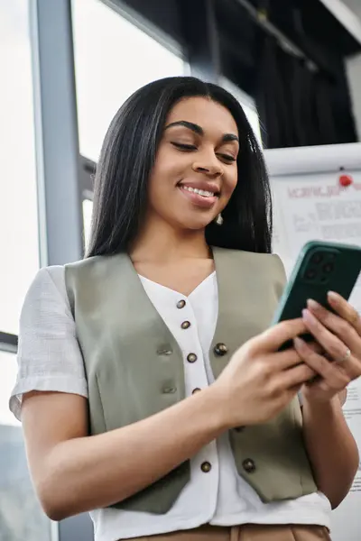 Eine Frau lächelt, während sie ihr Smartphone in einem stilvollen Innenraum benutzt. — Stock Photo