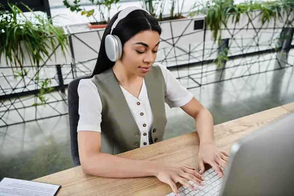 Concentrated woman typing on a laptop while listening to music in a lively workspace. — Stock Photo