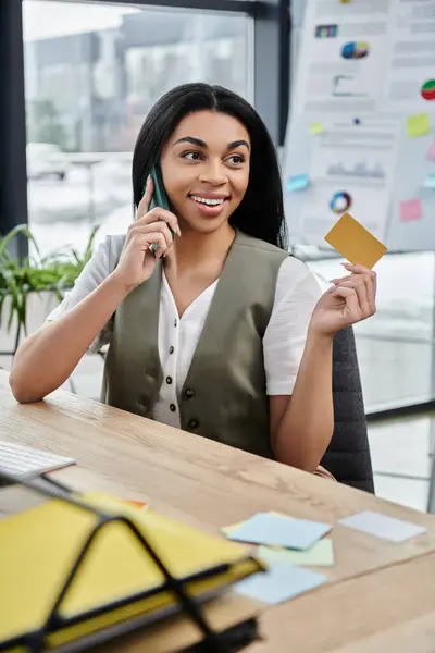A woman speaks on the phone while holding sticky notes at her desk. — Stock Photo