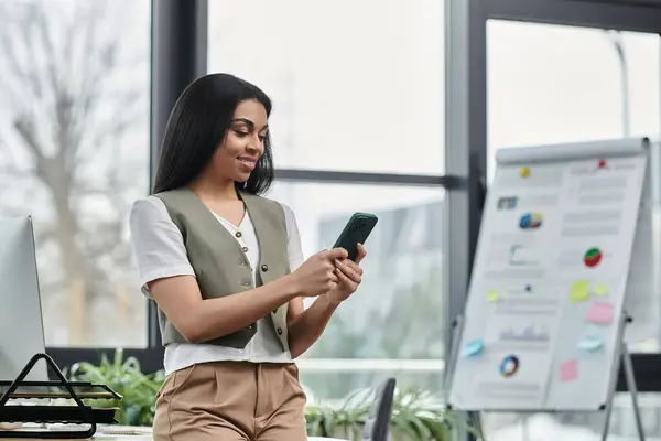 A stylish woman enjoys using her smartphone while standing in a contemporary workspace. — Stock Photo