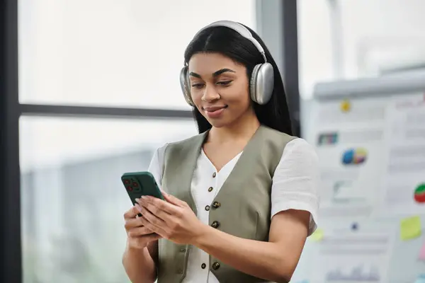 Listening to music, she smiles while browsing her phone in a vibrant workspace. — Stock Photo