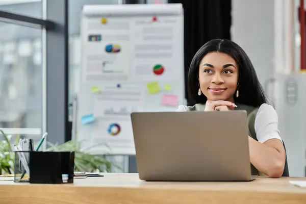 Una mujer reflexiva reflexiona mientras trabaja en su escritorio en un espacio de trabajo vibrante. - foto de stock
