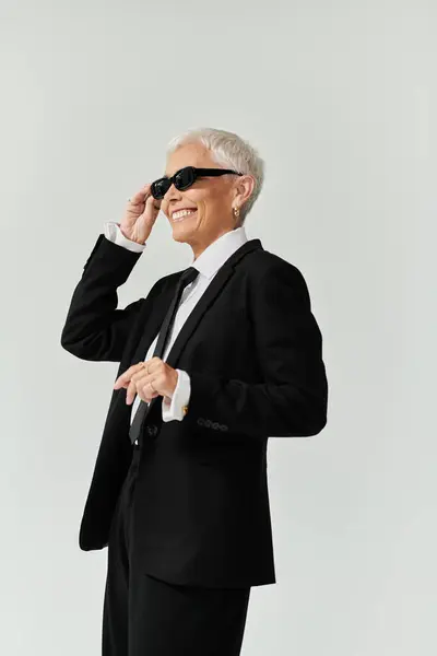 Confident woman smiles while adjusting her sunglasses in chic outfit. — Stock Photo