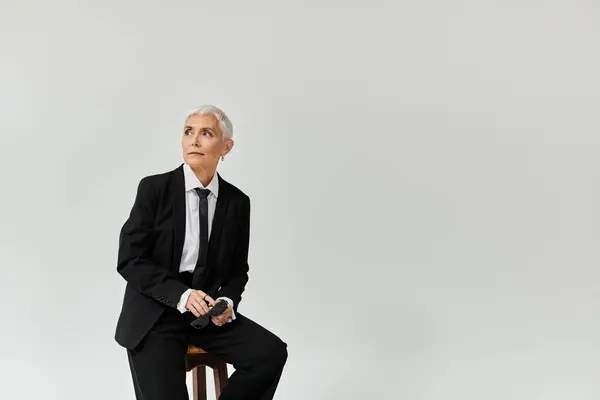 Mature woman gazes thoughtfully while dressed in sleek, stylish fashion. — Stock Photo