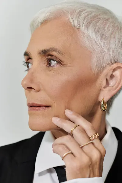 A mature woman with short hair exudes elegance in chic attire and gold accessories. — Stock Photo