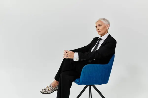 Mature woman with short hair exudes elegance while seated in a blue chair. — Stock Photo