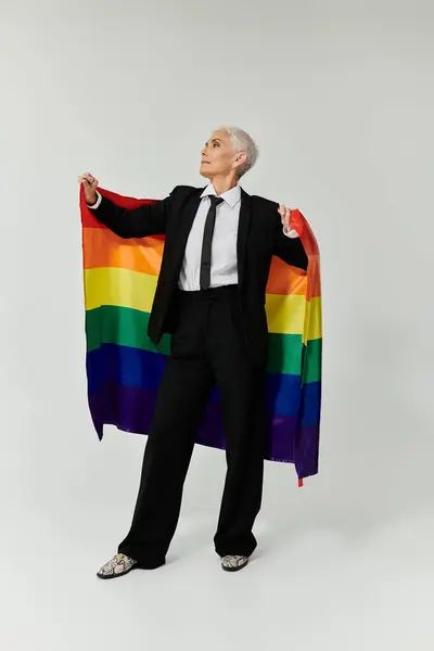 Confident woman showcases Pride spirit with a rainbow flag and sharp attire. — Stock Photo