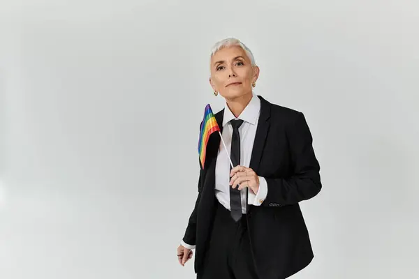 A mature woman showcases her pride in elegant attire holding a rainbow flag. — Stock Photo