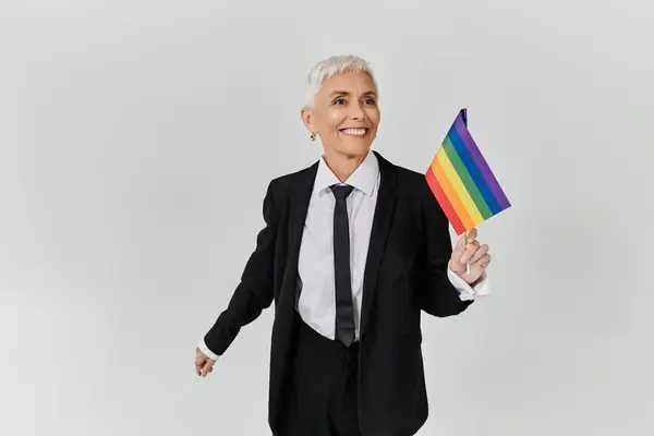 Eine reife Lesbe schwenkt freudig eine Regenbogenfahne in eleganter Kleidung. — Stockfoto