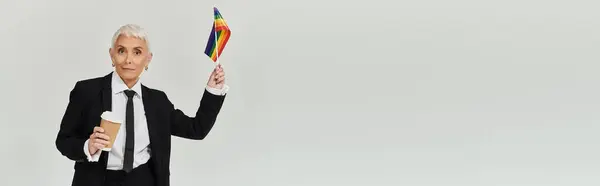 Dressed elegantly, a woman waves a pride flag while enjoying her coffee. — Stock Photo