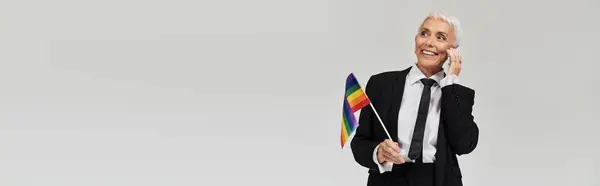 A stylish woman joyfully chats on her phone while waving a rainbow flag. — Stock Photo